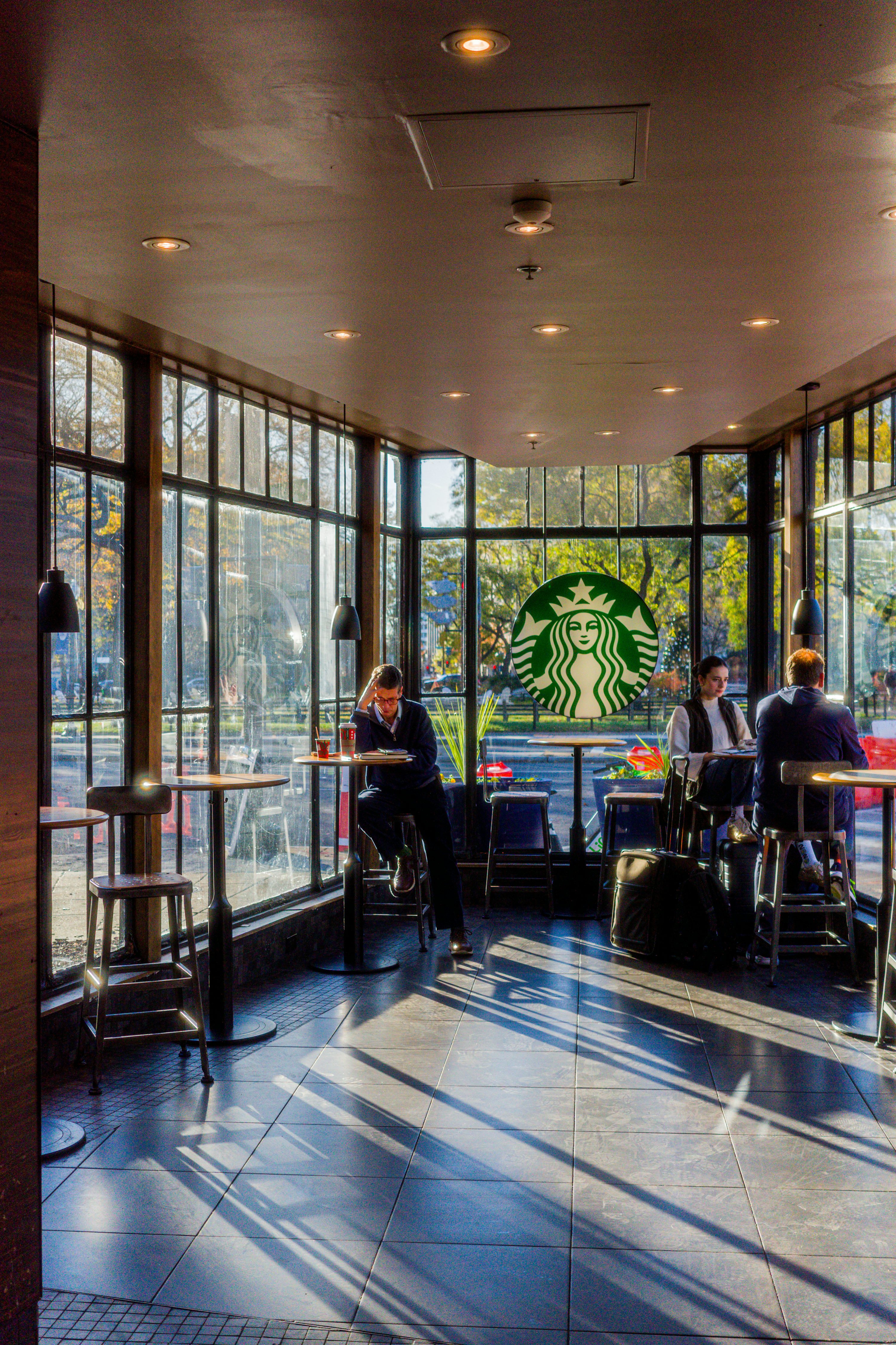 Interiér kavárny Starbucks s logem sirény na okně a hosty u stolků